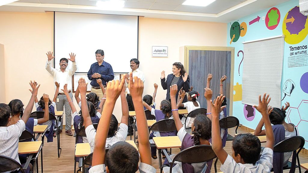 Classroom with pupils hands raised. Teachers seen smiling at the front.