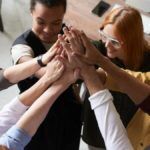 Team with hands all coming together in the middle of a circle. 