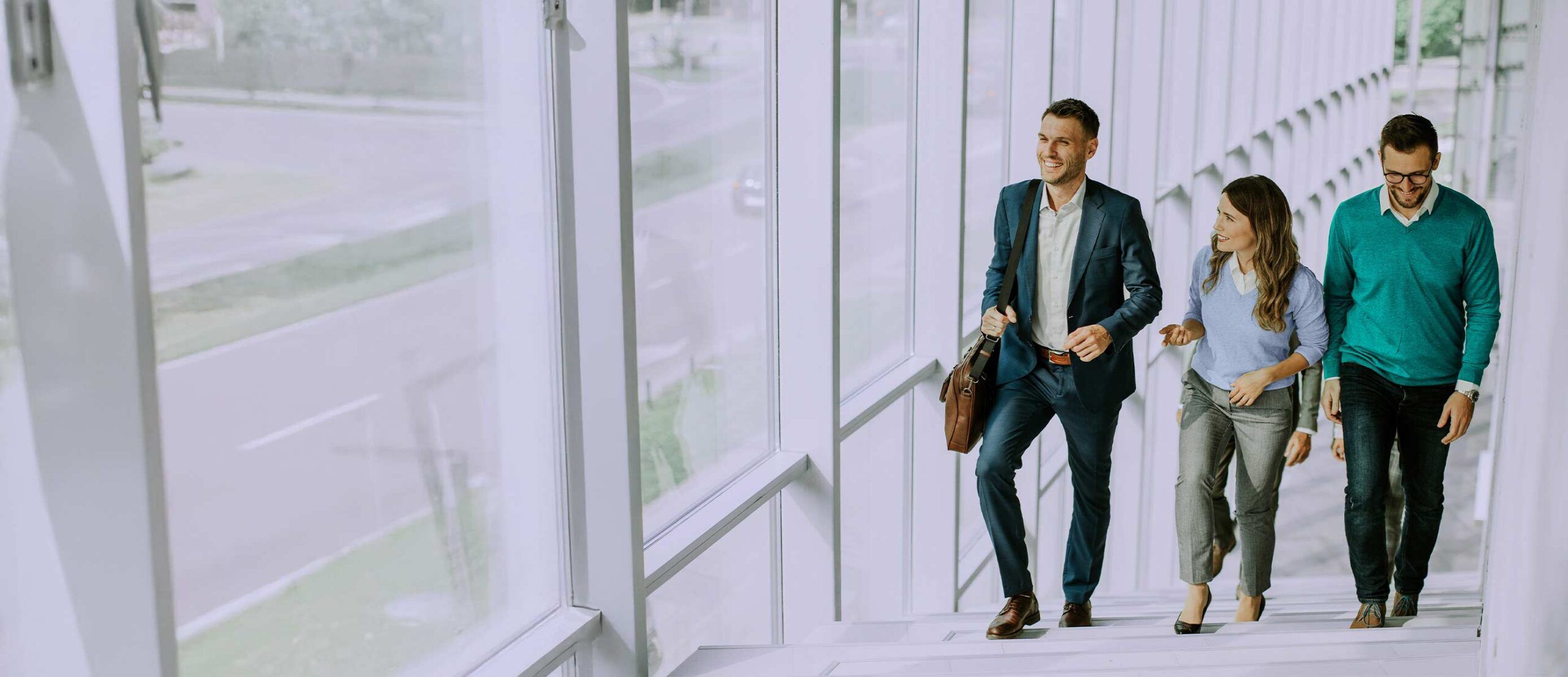 Three people walking up the stairs in an office building chatting.